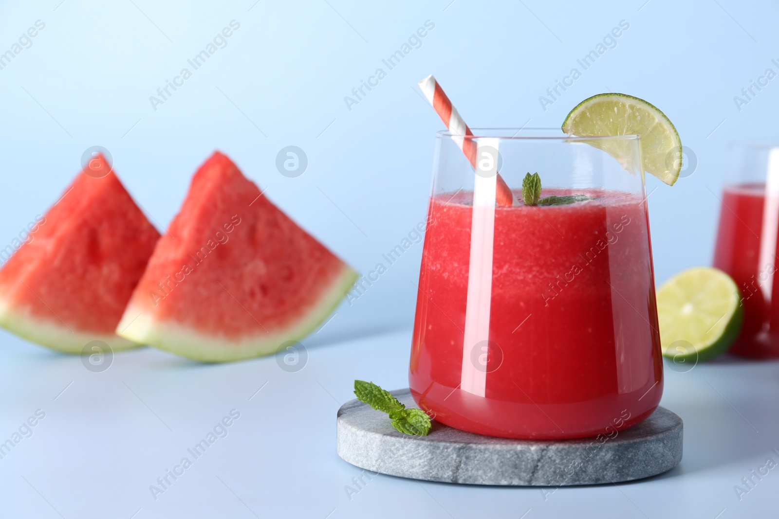 Photo of Tasty watermelon drink in glass, fresh fruits and mint on light blue background, closeup