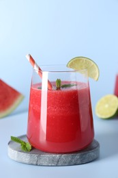 Photo of Tasty watermelon drink in glass, mint and fresh fruit on light blue background