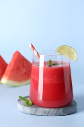 Photo of Tasty watermelon drink in glass, mint and fresh fruits on light blue background