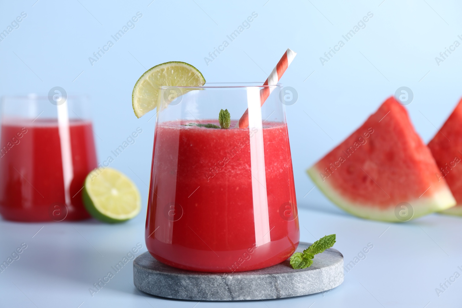 Photo of Tasty watermelon drink in glasses, fresh fruits and mint on light blue background, closeup