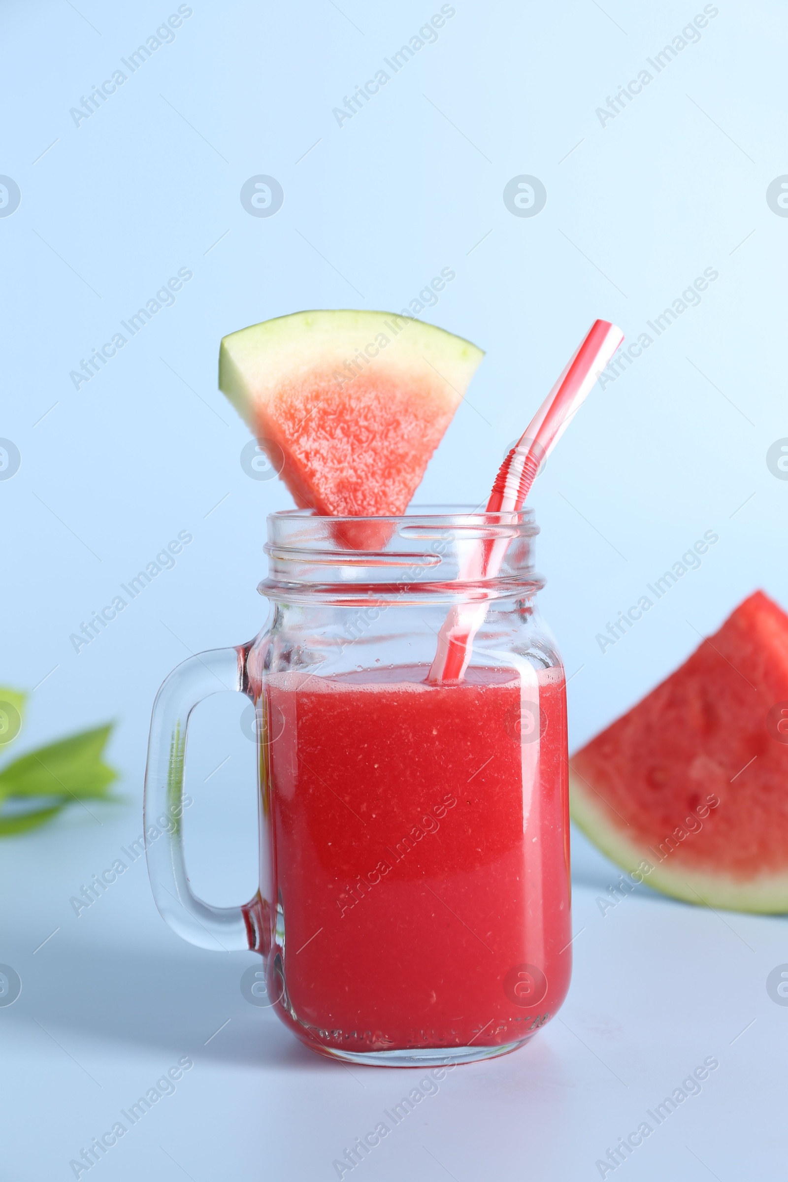 Photo of Tasty watermelon drink in mason jar, mint and fresh fruit on light blue background