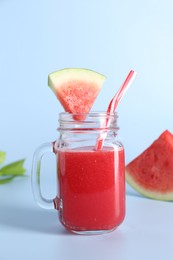 Photo of Tasty watermelon drink in mason jar, mint and fresh fruit on light blue background