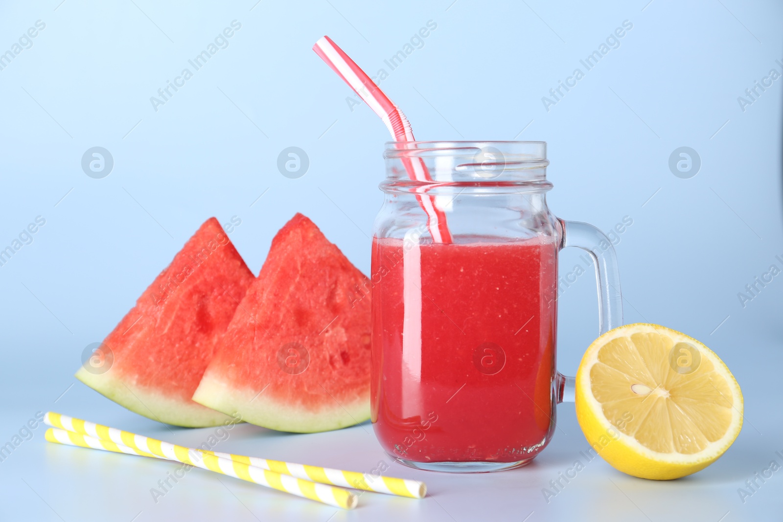 Photo of Tasty watermelon drink in mason jar, fresh fruits and straws on light blue background