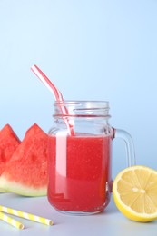 Photo of Tasty watermelon drink in mason jar, fresh fruits and straws on light blue background