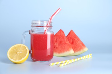 Photo of Tasty watermelon drink in mason jar, fresh fruits and straws on light blue background