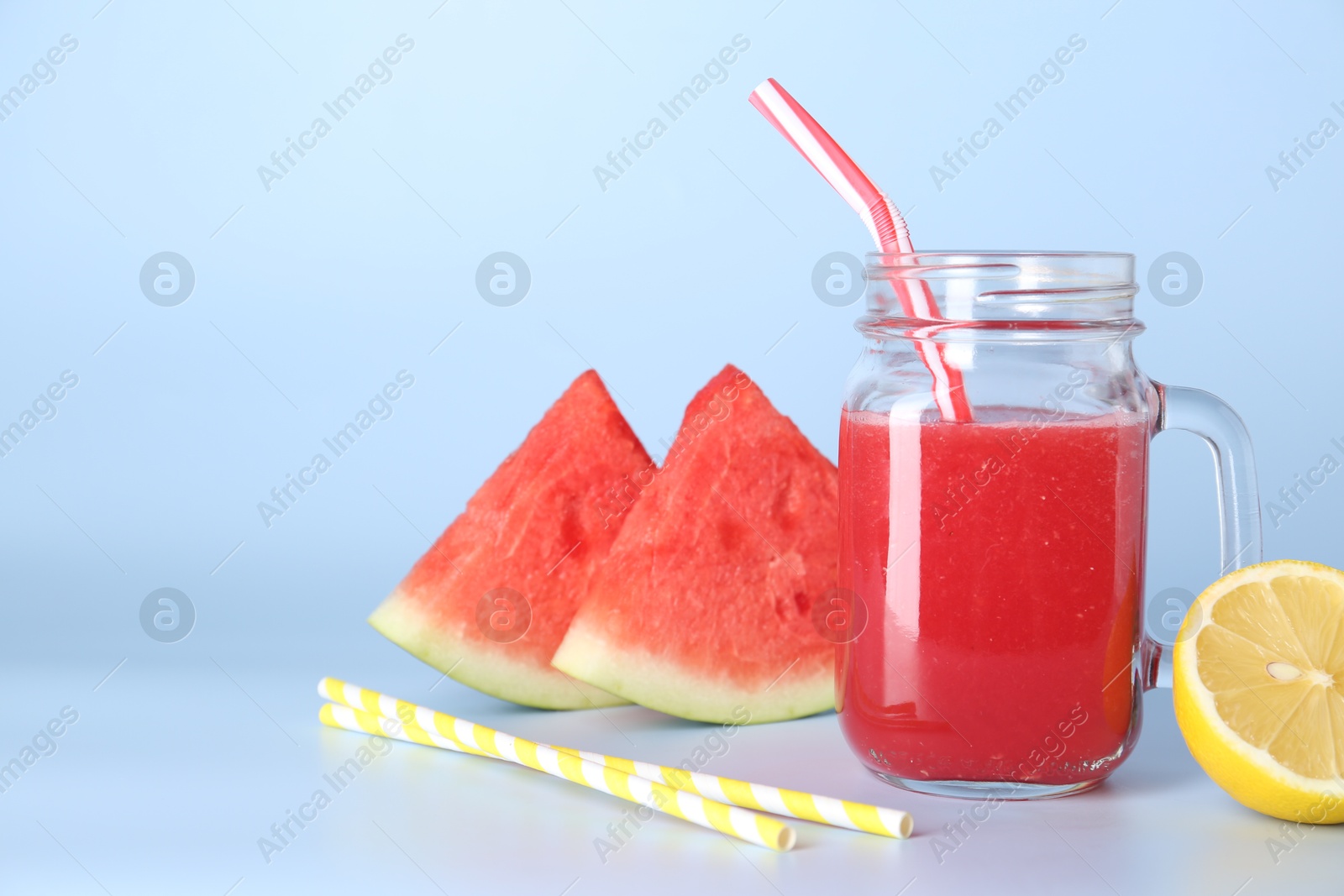 Photo of Tasty watermelon drink in mason jar, fresh fruits and straws on light blue background