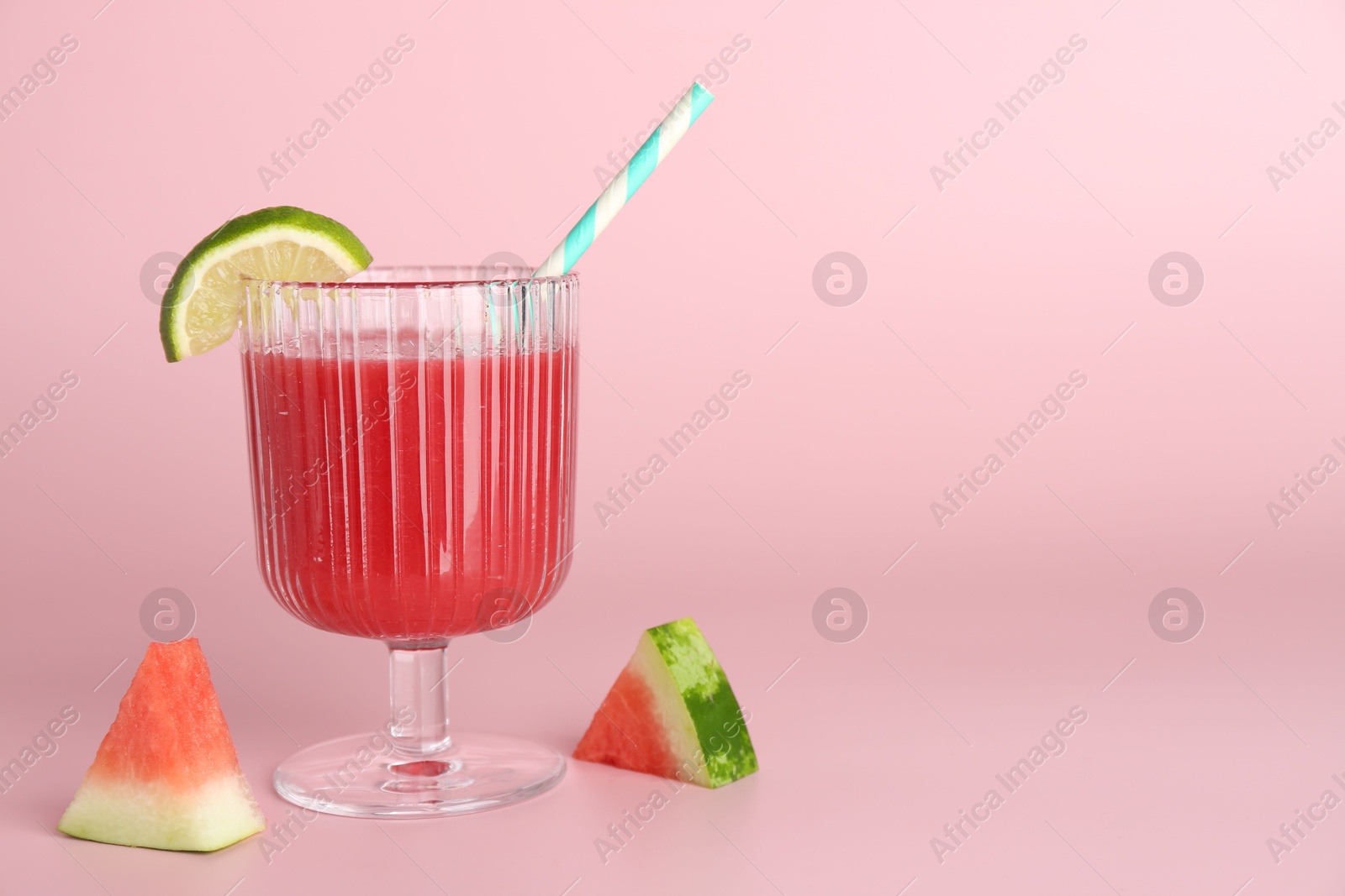 Photo of Tasty watermelon drink in glass and fresh fruits on pink background, space for text