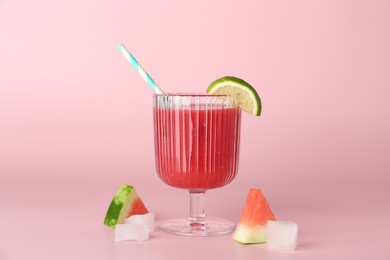 Photo of Tasty watermelon drink in glass, fresh fruits and ice cubes on pink background