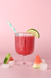 Photo of Tasty watermelon drink in glass, fresh fruits and ice cubes on pink background