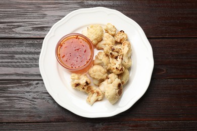 Photo of Plate with baked cauliflower and sauce on wooden table, top view