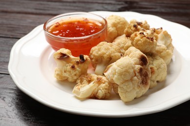 Plate with baked cauliflower and sauce on wooden table, closeup