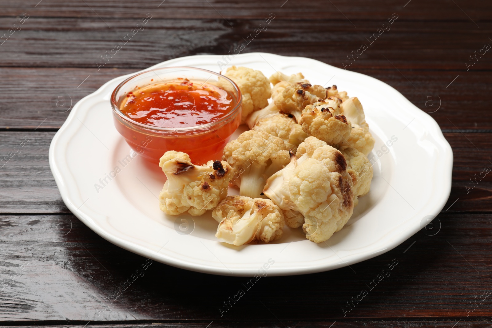 Photo of Plate with baked cauliflower and sauce on wooden table