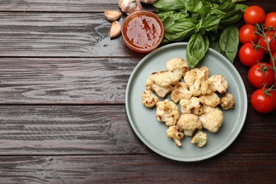 Photo of Plate with baked cauliflower, products and sauce on wooden table, flat lay. Space for text