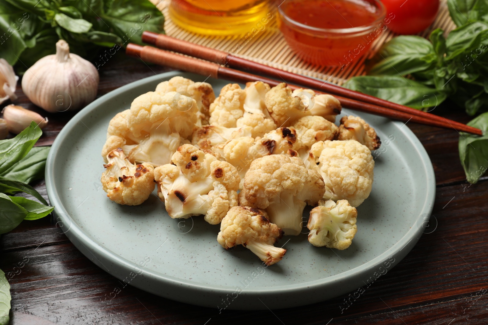 Photo of Plate with baked cauliflower, products, chopsticks and sauce on wooden table