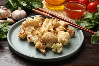 Plate with baked cauliflower, products, chopsticks and sauce on wooden table