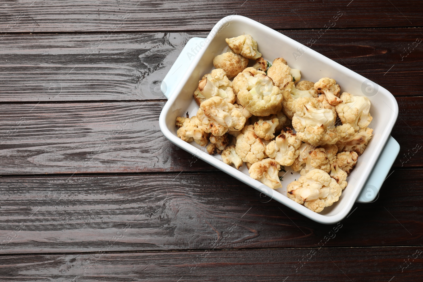 Photo of Baked cauliflower in baking dish on wooden table, top view. Space for text