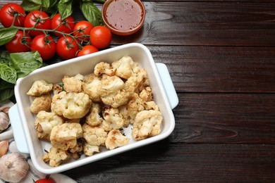 Baked cauliflower in baking dish, sauce and products on wooden table, flat lay. Space for text