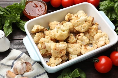 Baked cauliflower in baking dish, sauce and products on wooden table