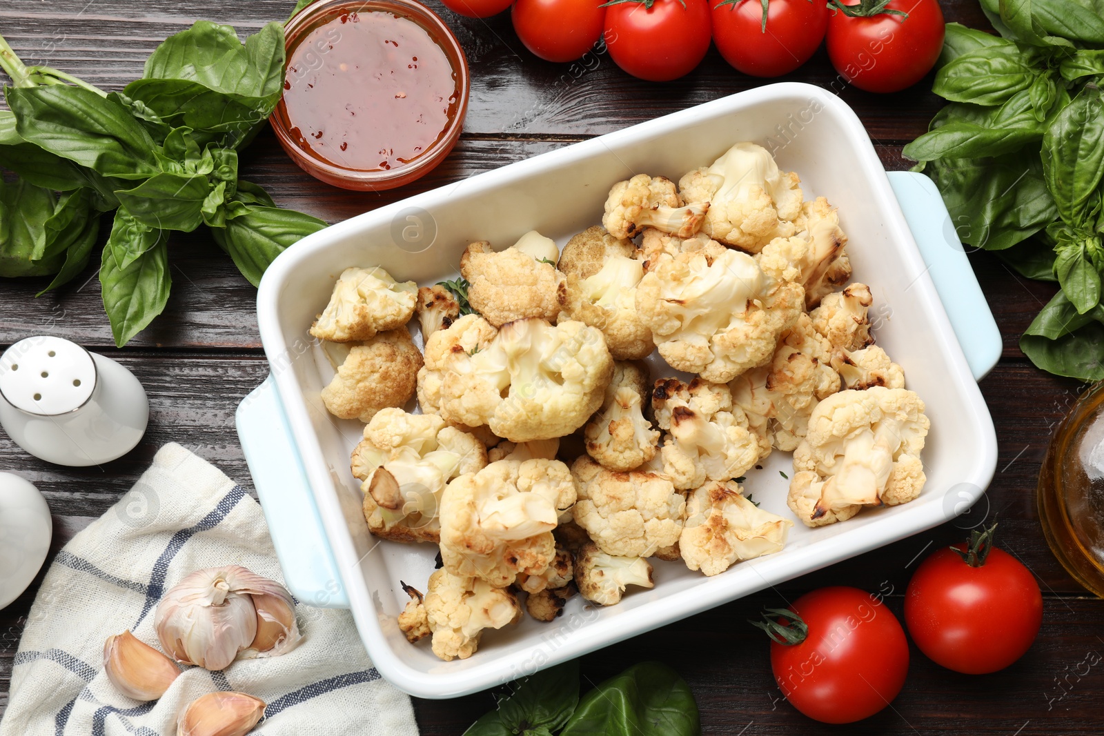 Photo of Baked cauliflower in baking dish, sauce and products on wooden table, flat lay