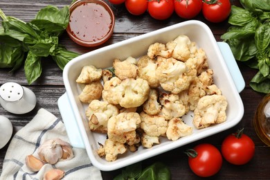 Baked cauliflower in baking dish, sauce and products on wooden table, flat lay