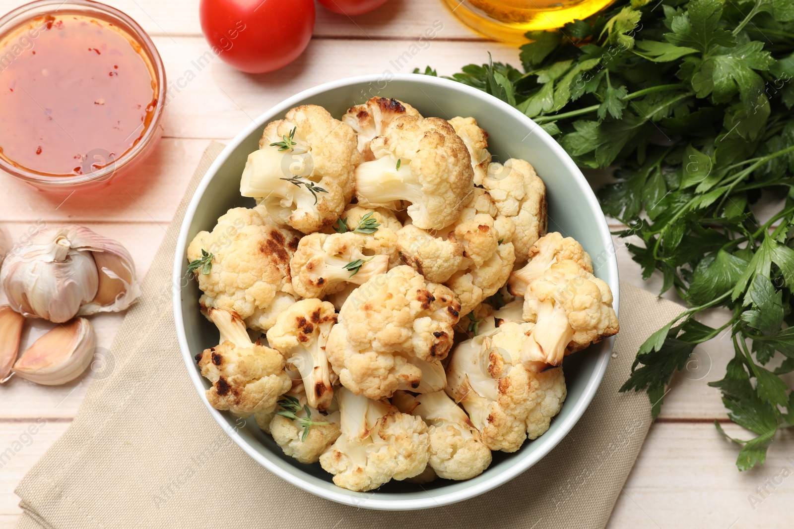 Photo of Baked cauliflower in bowl, sauce and products on light wooden table, flat lay