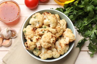 Baked cauliflower in bowl, sauce and products on light wooden table, flat lay