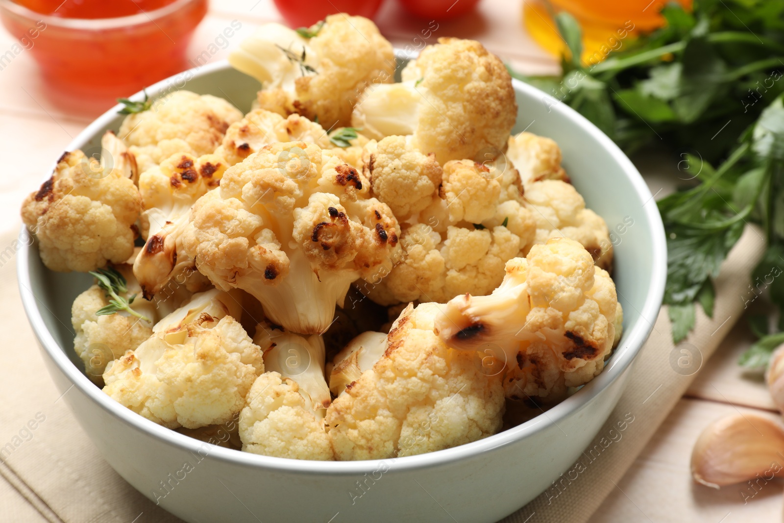 Photo of Baked cauliflower in bowl, sauce and products on light wooden table, closeup