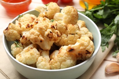 Baked cauliflower in bowl, sauce and products on light wooden table, closeup