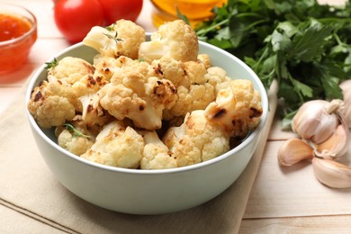 Baked cauliflower in bowl, sauce and products on light wooden table