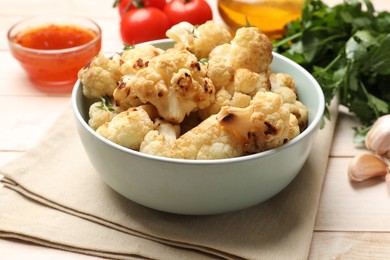 Photo of Baked cauliflower in bowl, sauce and products on light wooden table