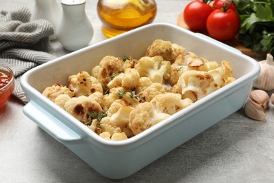 Photo of Baked cauliflower, products and sauce on light grey table, closeup