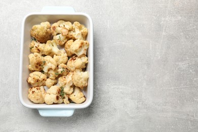 Baked cauliflower in baking dish on light grey table, top view. Space for text