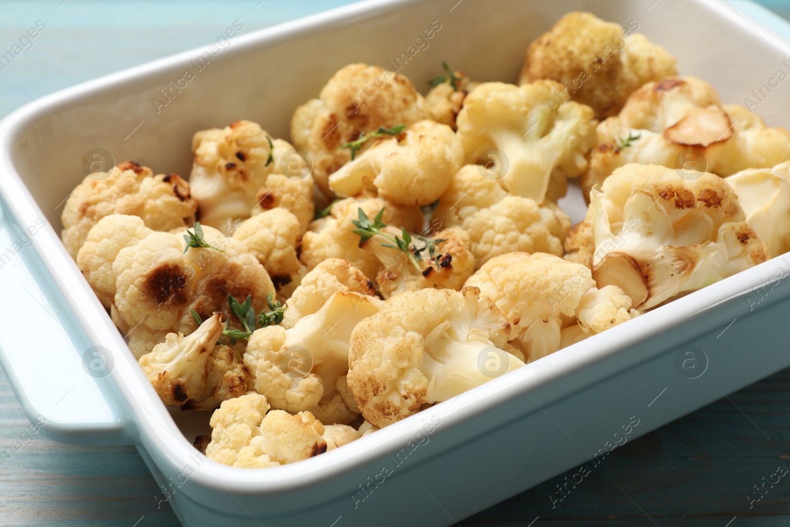 Photo of Baked cauliflower in baking dish on light blue wooden table, closeup