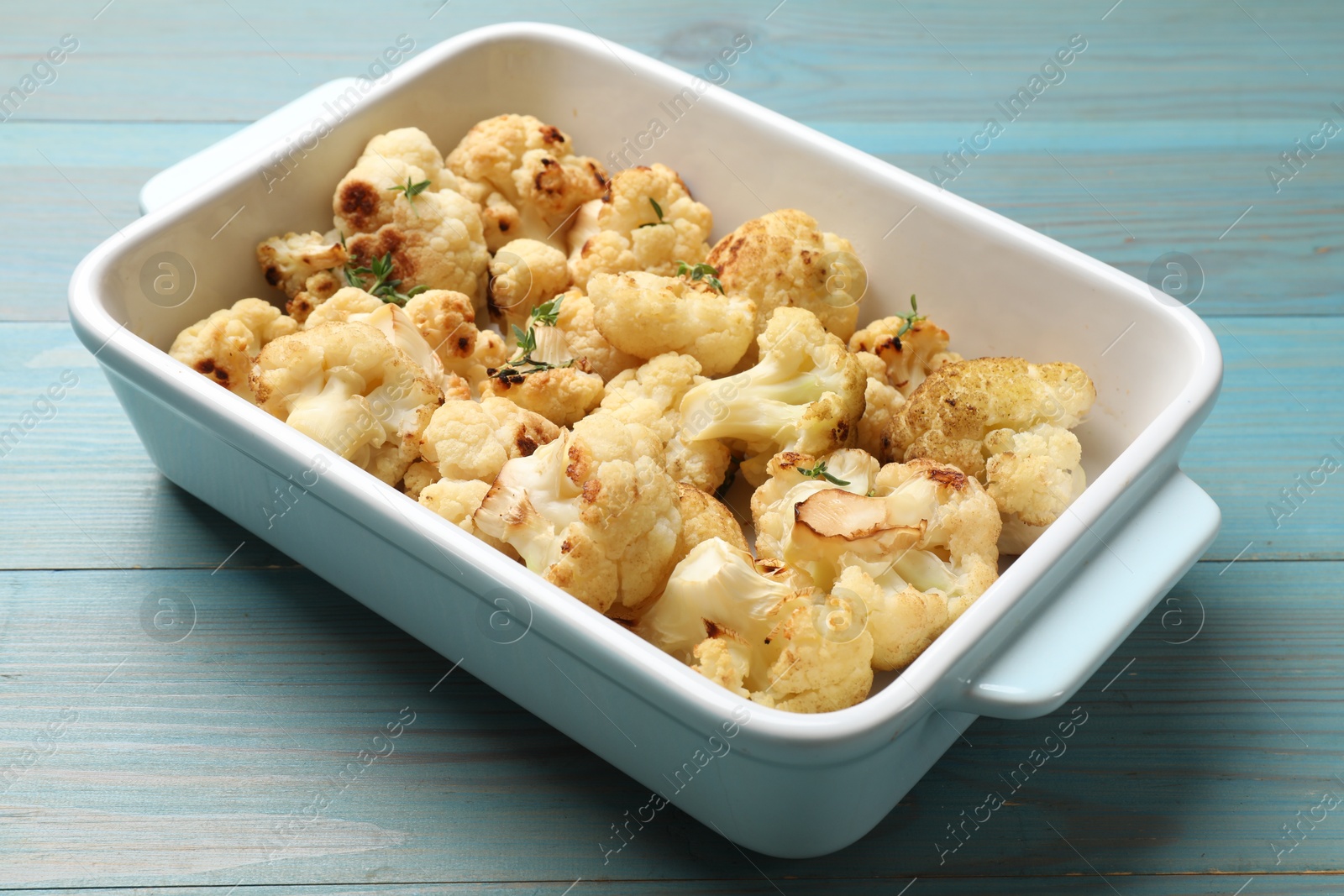 Photo of Baked cauliflower in baking dish on light blue wooden table