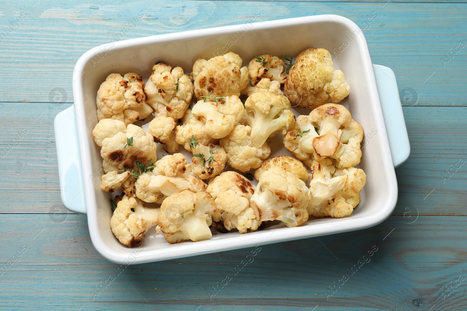 Photo of Baked cauliflower in baking dish on light blue wooden table, top view