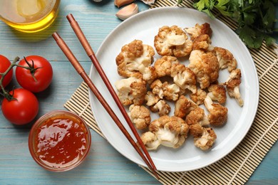 Photo of Baked cauliflower, products and sauce on light blue wooden table, flat lay