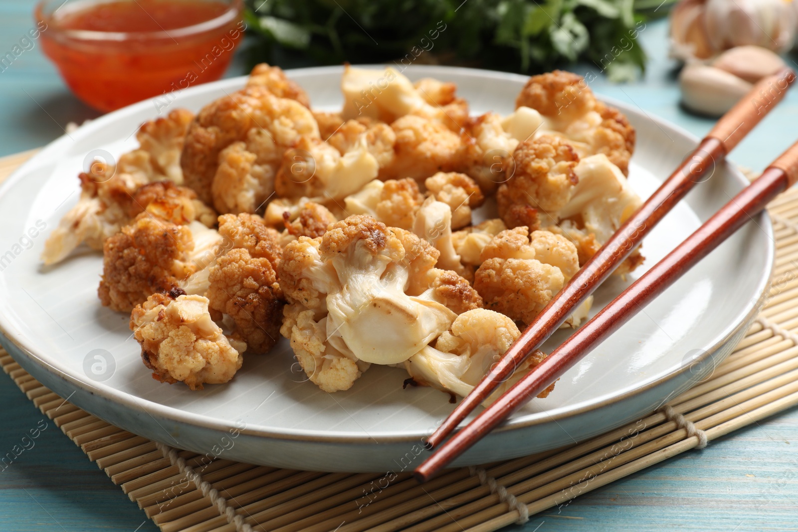 Photo of Baked cauliflower, products and sauce on light blue wooden table, closeup