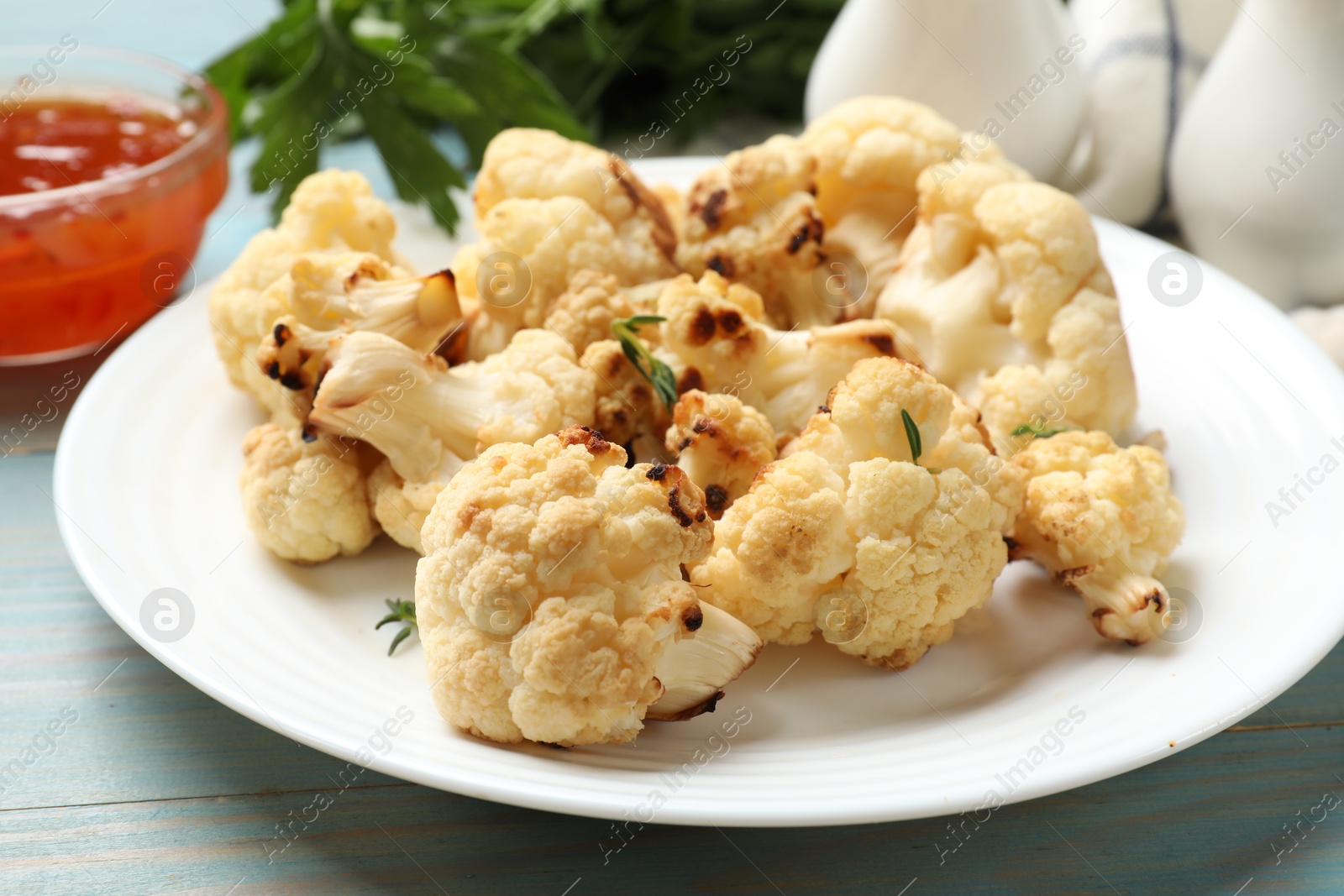 Photo of Baked cauliflower and sauce on light blue wooden table, closeup