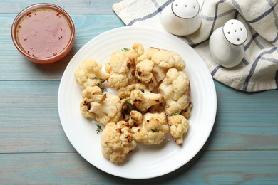 Photo of Baked cauliflower and sauce on light blue wooden table, top view