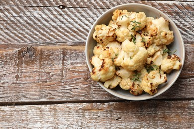 Photo of Baked cauliflower in bowl on wooden table, top view. Space for text