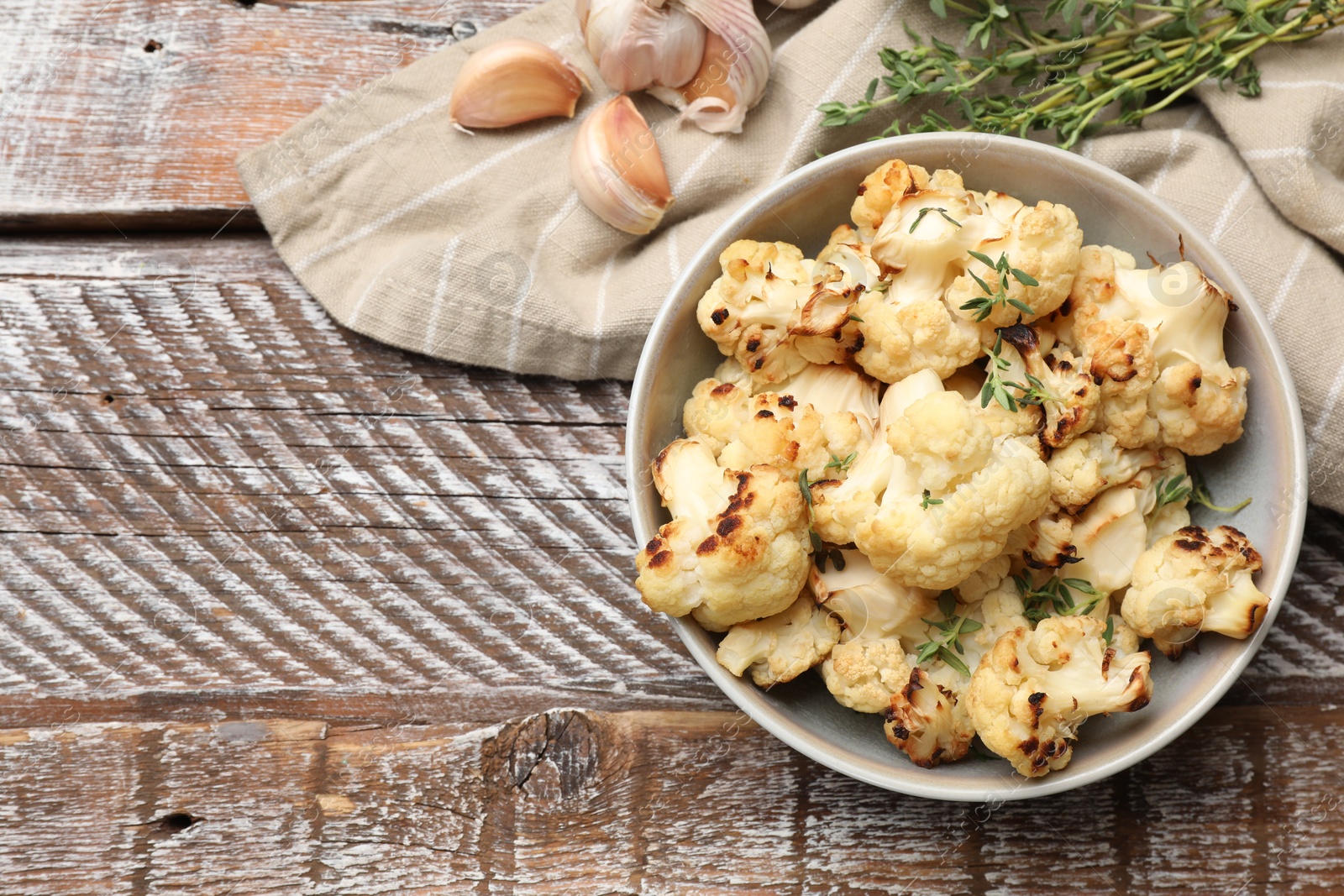 Photo of Baked cauliflower in bowl, garlic and thyme on wooden table, flat lay. Space for text