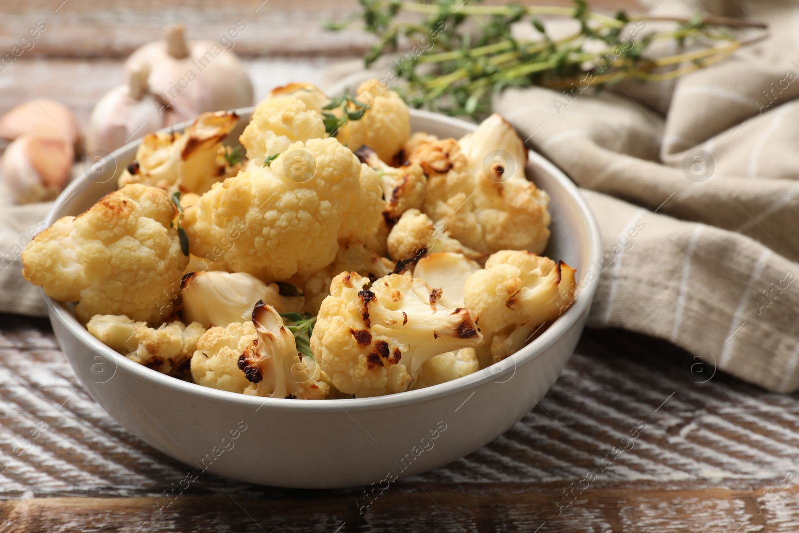 Photo of Baked cauliflower in bowl, garlic and thyme on wooden table