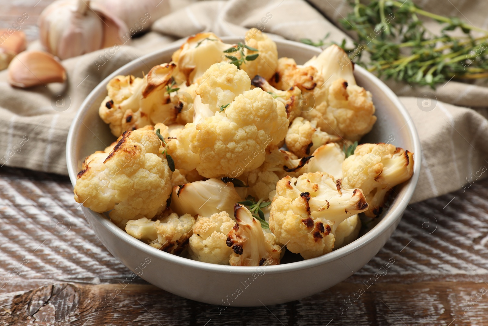 Photo of Baked cauliflower in bowl, garlic and thyme on wooden table