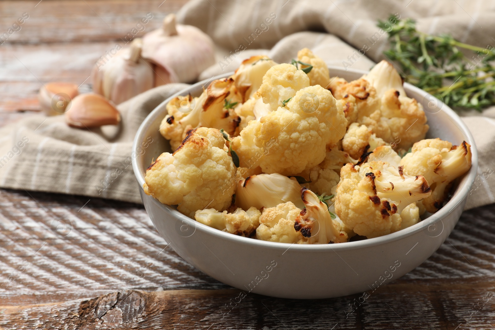 Photo of Baked cauliflower in bowl, garlic and thyme on wooden table