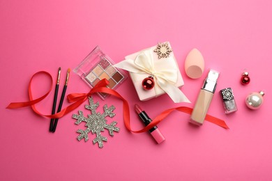 Flat lay composition with makeup products and Christmas decor on pink background