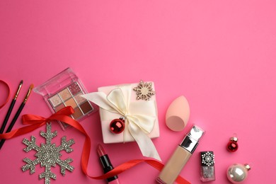 Flat lay composition with makeup products and Christmas decor on pink background. Space for text