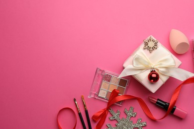 Flat lay composition with makeup products and Christmas decor on pink background. Space for text