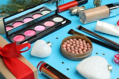 Photo of Different makeup products and Christmas decor on light blue background, closeup