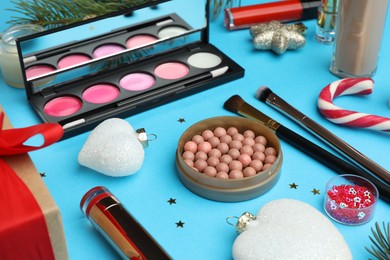 Photo of Different makeup products and Christmas decor on light blue background, closeup