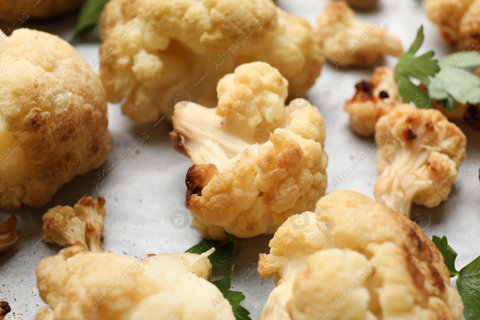 Photo of Tasty baked cauliflower and parsley on parchment, closeup